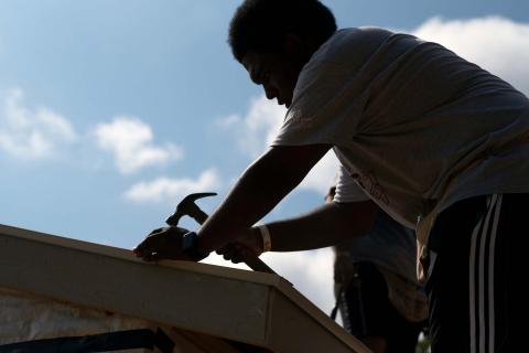 A volunteer hammers a nail into a roof for Service Dawgs and Habitat for Humanity
